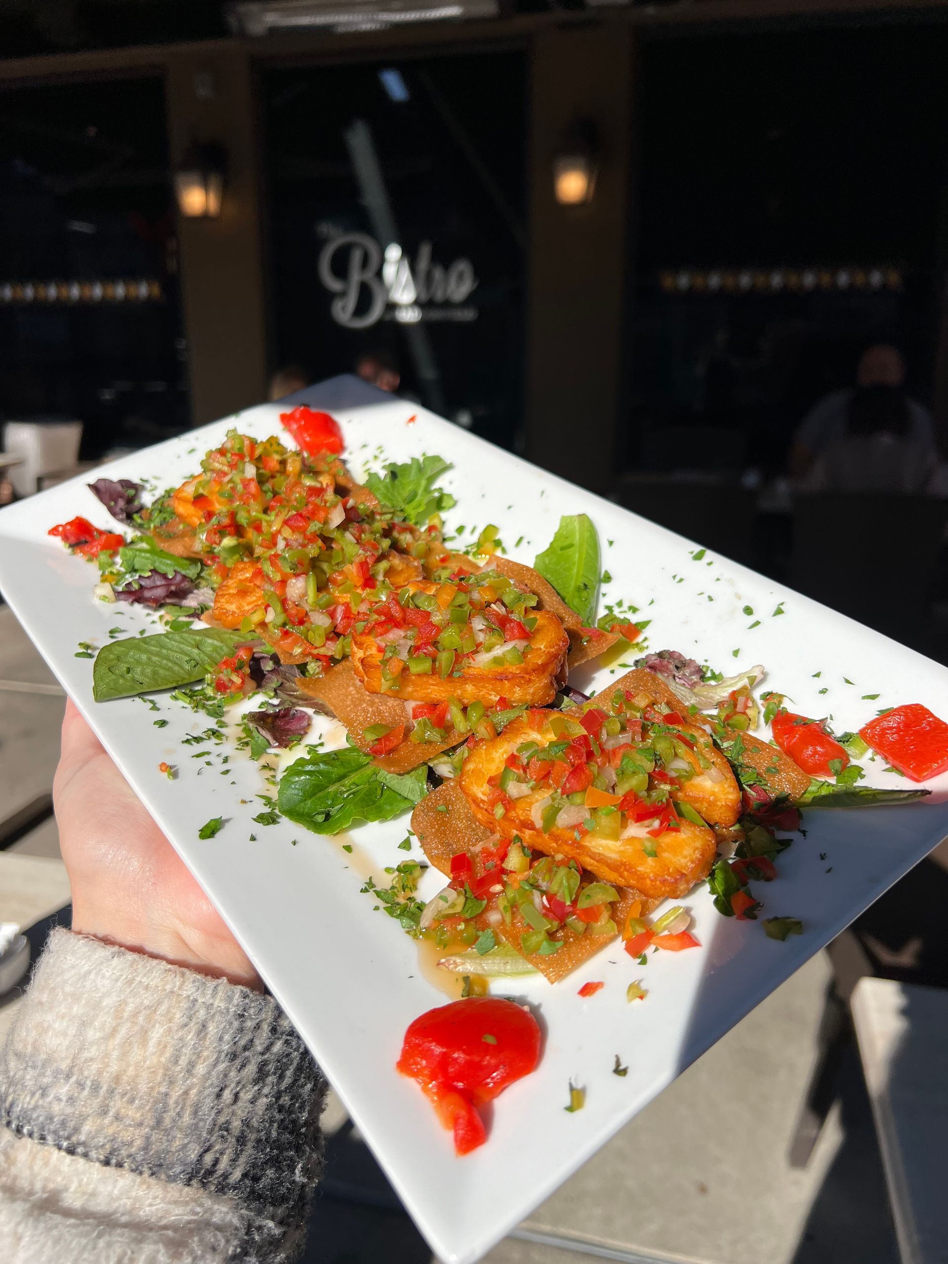 Plated colorful gourmet dish with herbs and sauce, held outdoors in front of a restaurant entrance