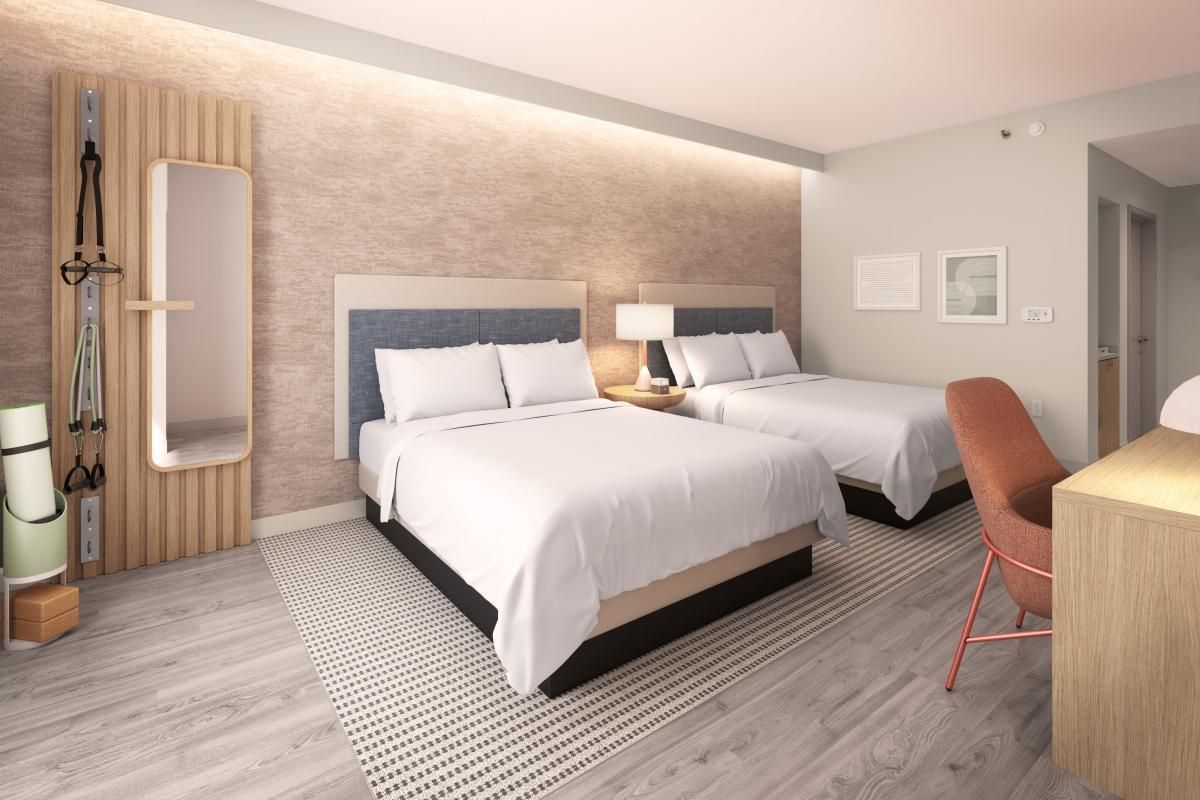 Modern hotel room with two white beds, bedside lamps, desk, and orange chair