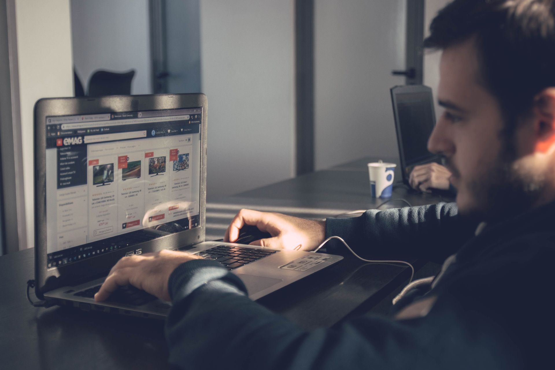 Person working on a laptop in a dimly lit office, looking at a website on the screen