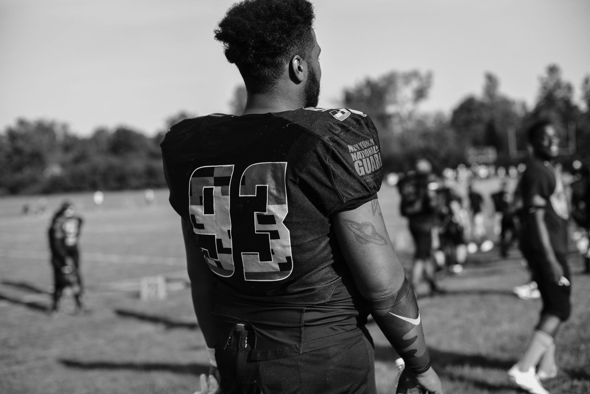 Football player wearing jersey number 93 stands on a field, looking towards teammates.