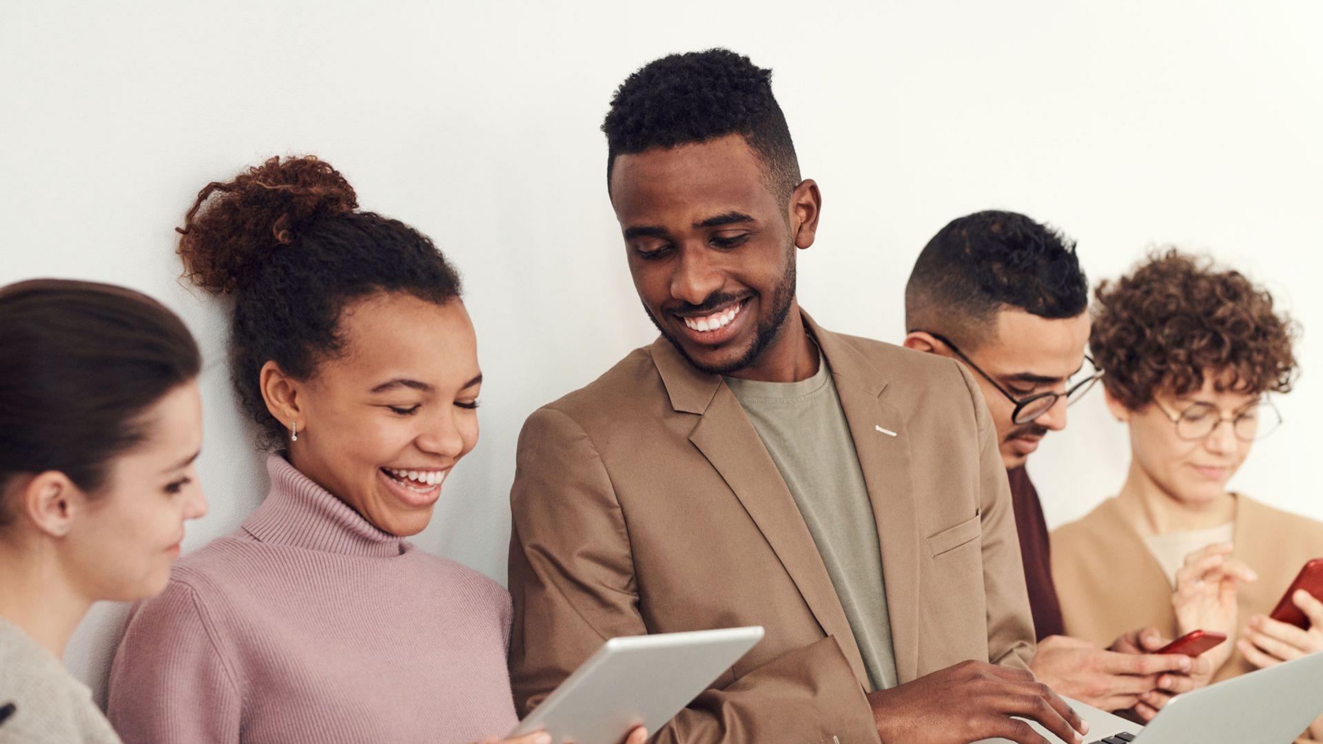 Group of coworkers smiling and using tablets in a bright office setting