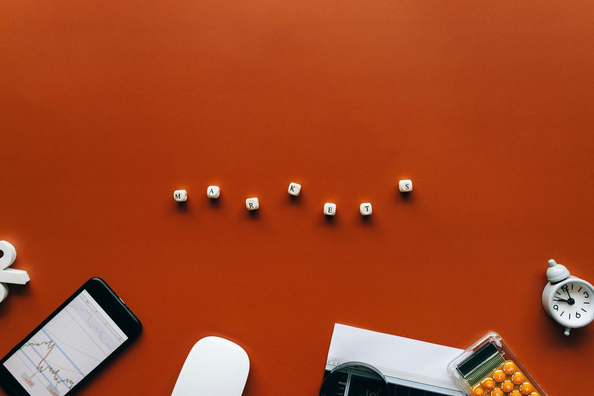 Orange desk with scattered stationery, a phone, earbuds, a clock, and dice arranged in a line