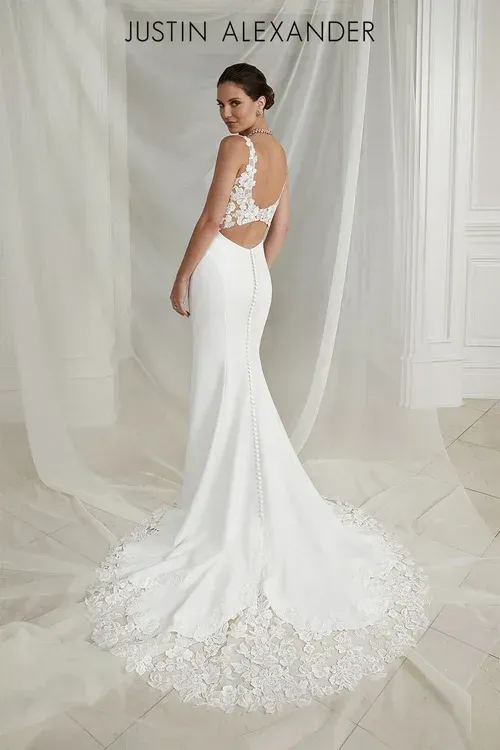 Woman in a white wedding dress with lace back and train, standing in a light-filled room.