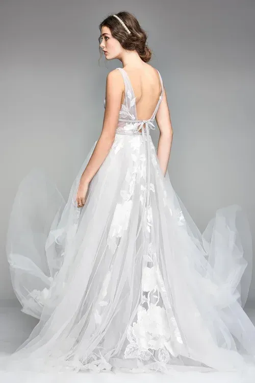 Woman in a flowing white wedding dress, back view, with open back and long train.