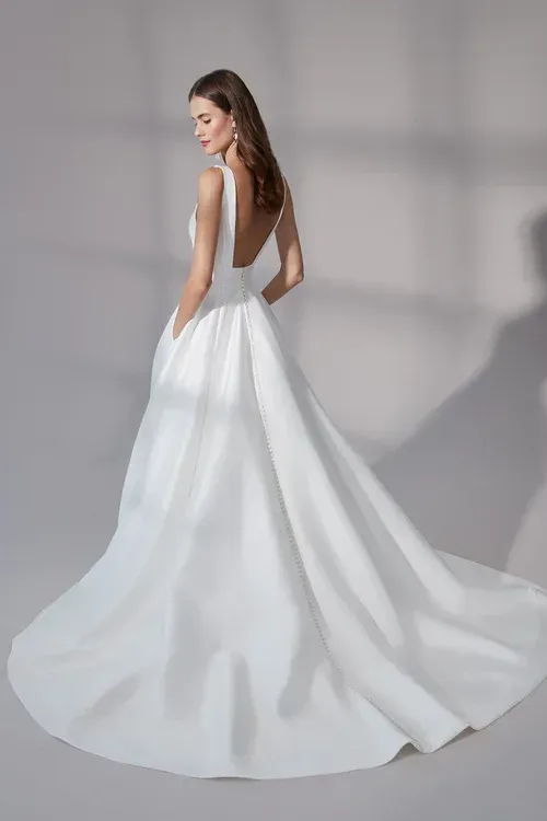 Woman in a white wedding dress with a low back, pockets, and a long train, standing in a studio.