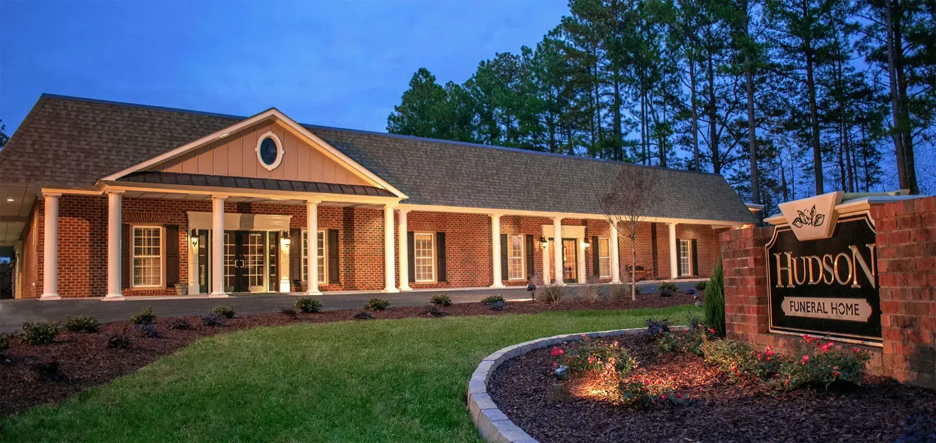 Brick office building at dusk with lit windows and a sign in front reading “HAYON”