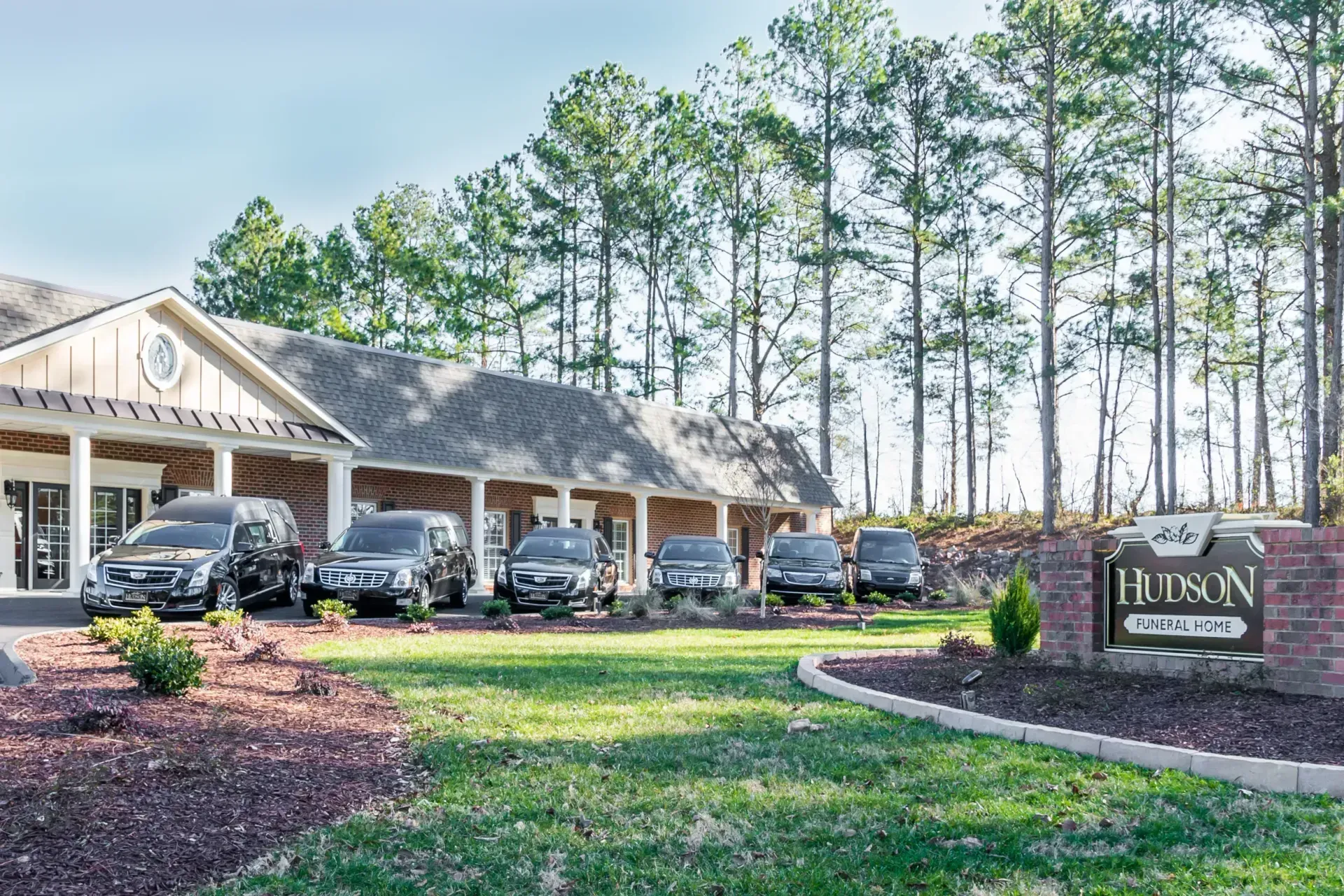 Lawn sign outside a lodge-style building with parked cars and tall pine trees in front