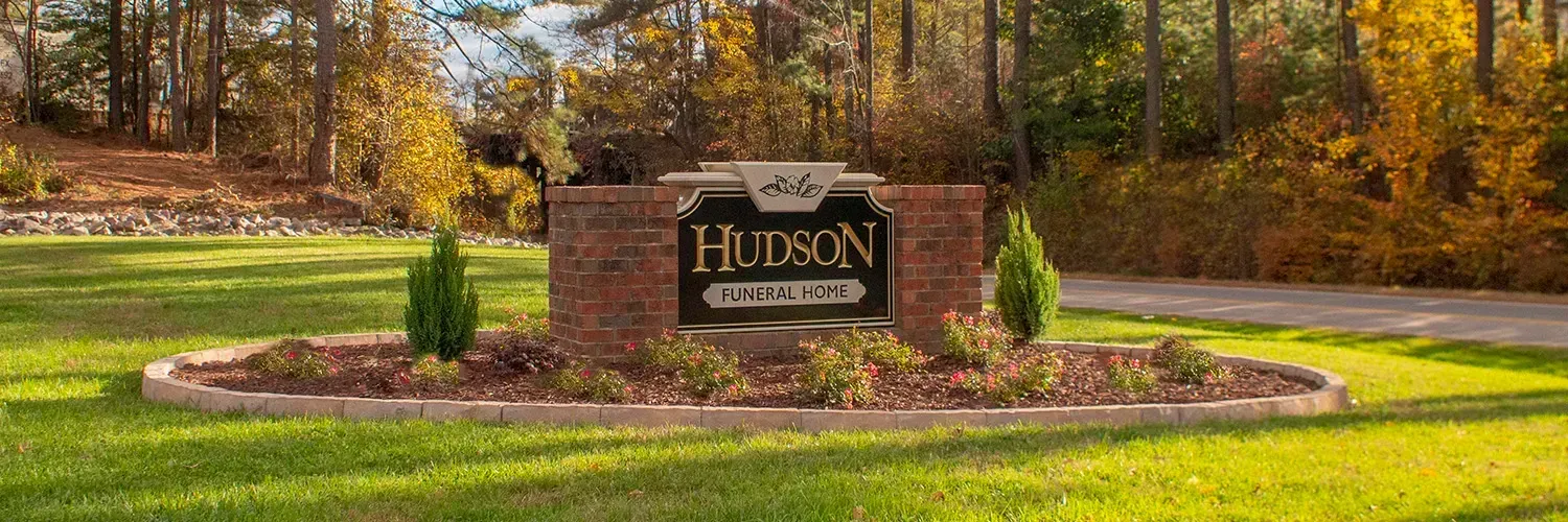 Stone entrance sign for a neighborhood, surrounded by green grass and autumn trees.