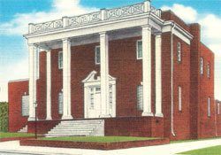 Red brick civic building with white columns and a stairway entrance under a blue sky