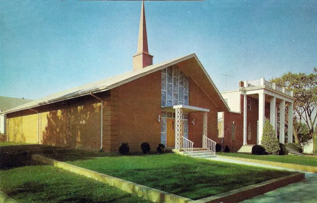 Brick church with tall steeple, white entrance, and green lawn under a blue sky