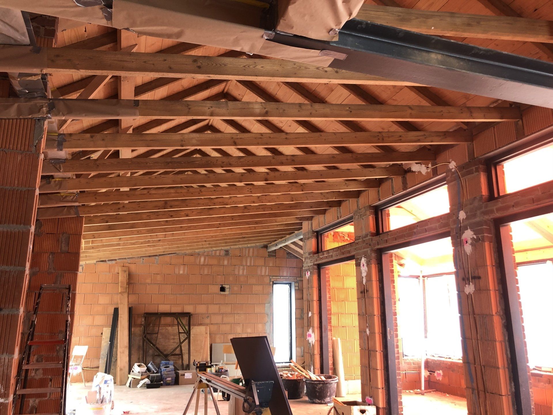 Een foto van een bouwplaats binnenshuis, met een onafgewerkte ruimte met een zichtbaar plafond met houten balken en bakstenen muren.