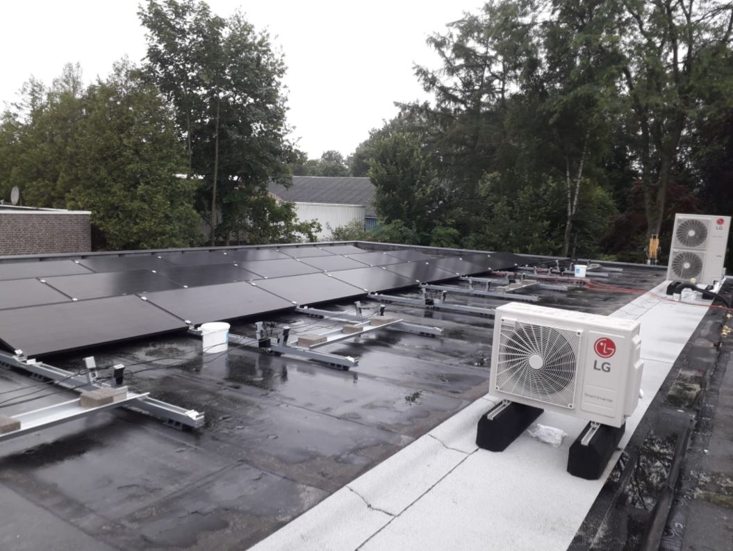 Een dak met zwarte zonnepanelen, elektriciteitsleidingen en twee LG-buitenunits voor de airconditioning op een bewolkte dag.
