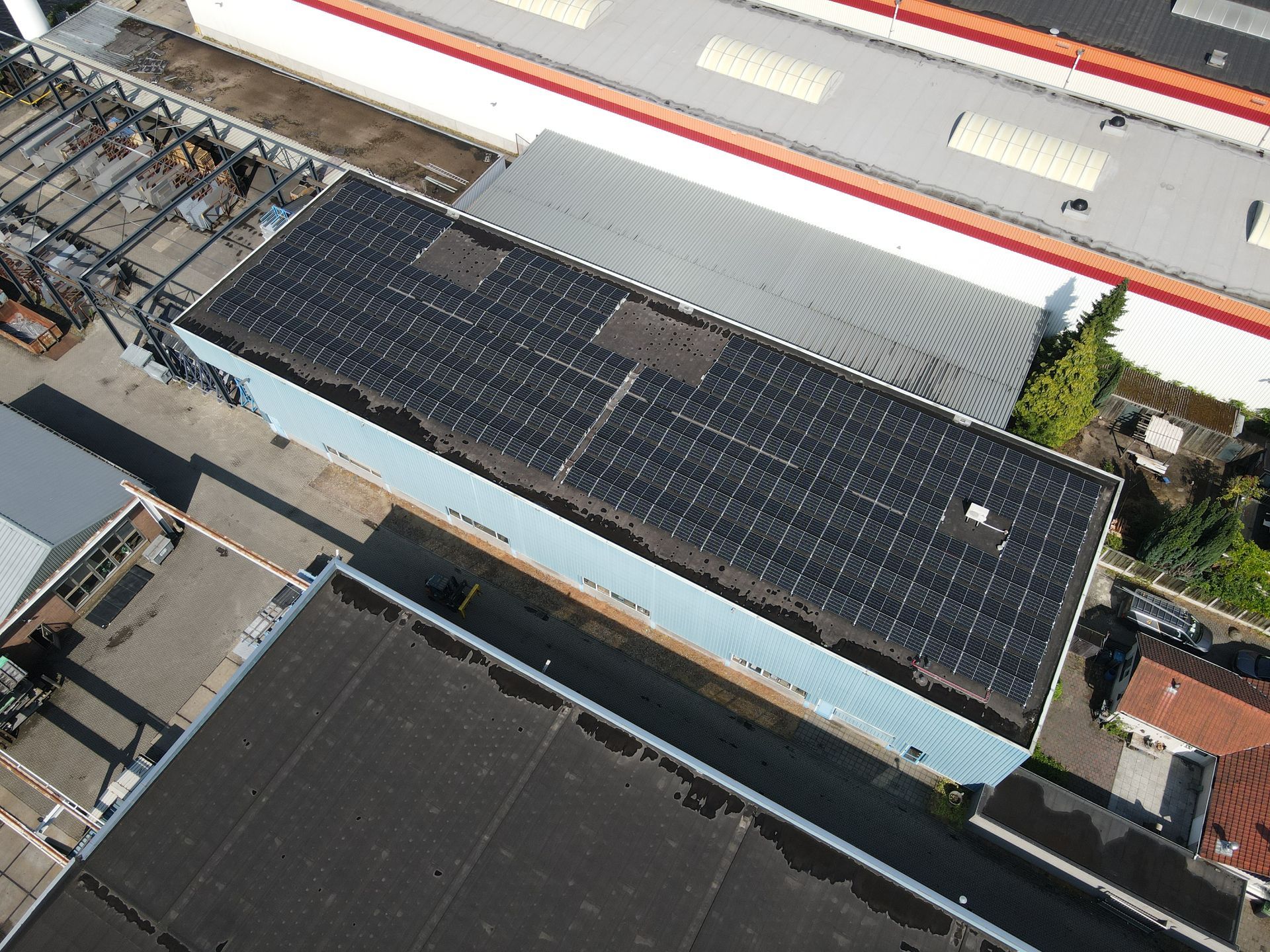Een luchtfoto van een gebouw met een grote zonnepaneleninstallatie op het dak, gelegen in een industriegebied.
