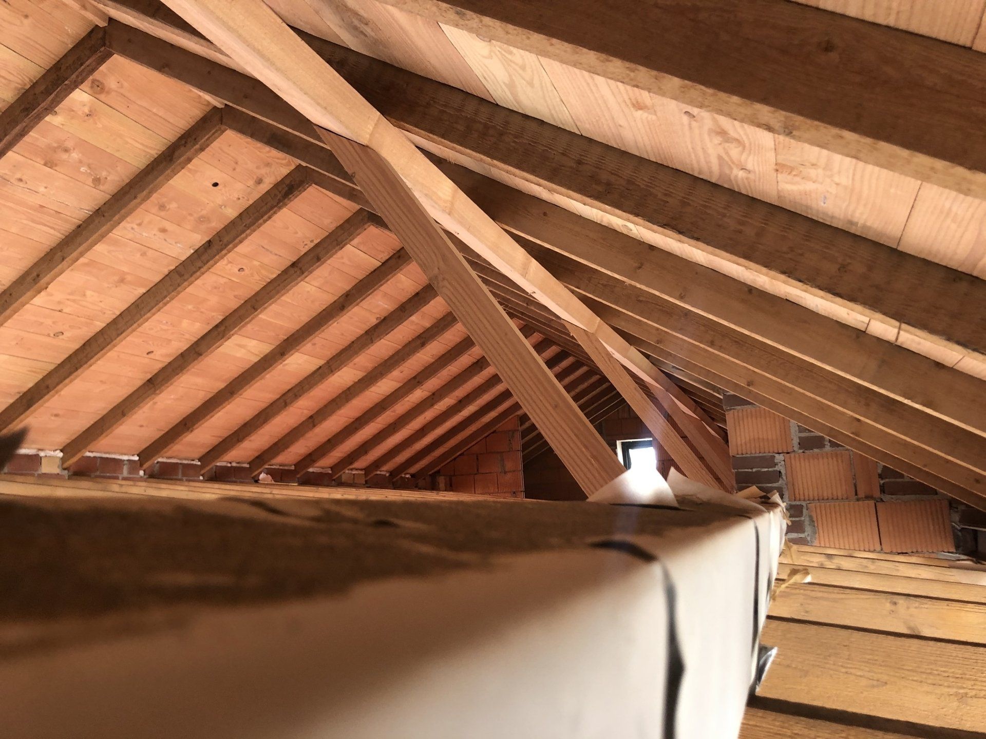 Zicht op een onafgewerkt houten zolderinterieur met zichtbare dakspanten, dakbeschot en isolatie langs de vloer.