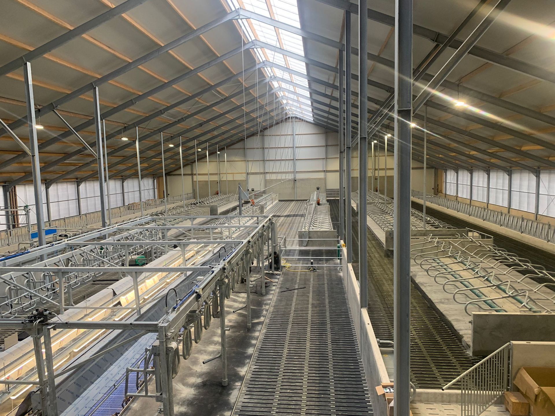 Een uitgestrekte, overdekte landbouwfaciliteit met metalen frames, voerbakken en rijen stallen onder een puntdak.