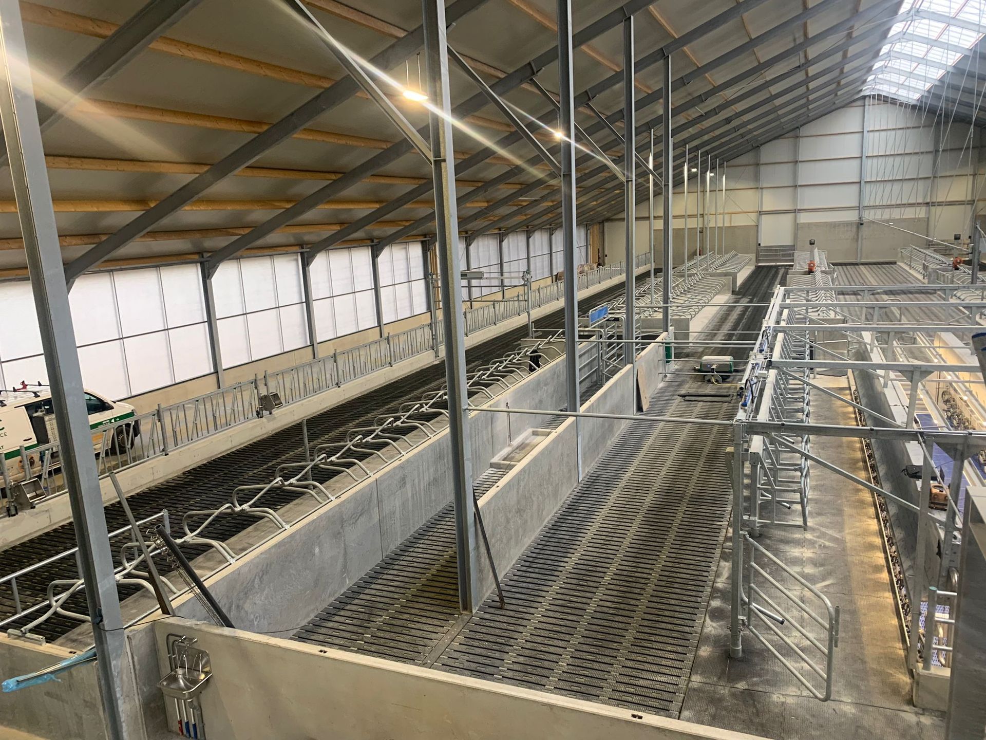 Een hoog perspectief van een moderne, lege veestal met metalen boxen, een betonnen vloer en een grote dakconstructie.