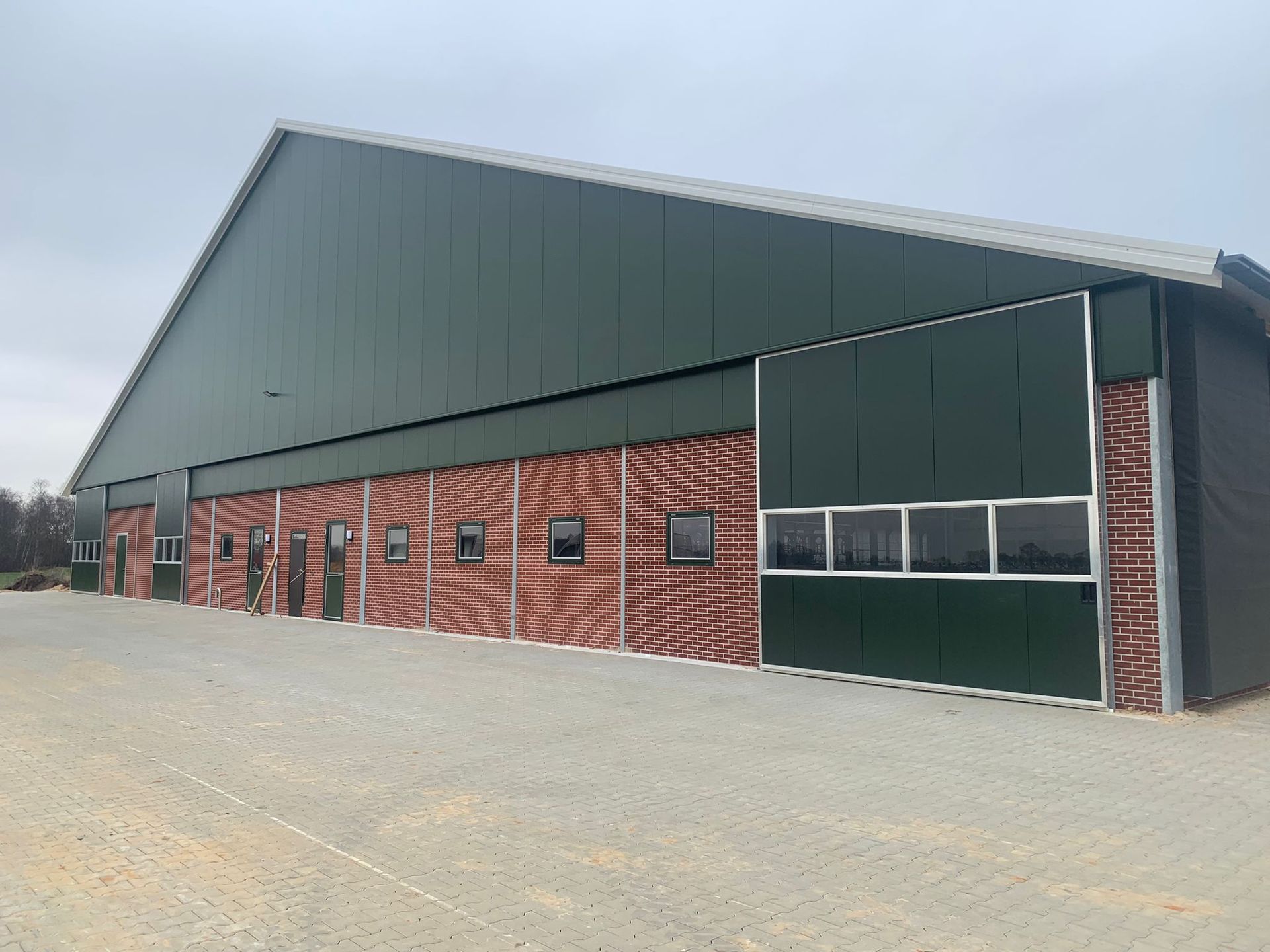Een groot, donkergroen industrieel gebouw met een oranje en bruin patroon en witte kozijnen.