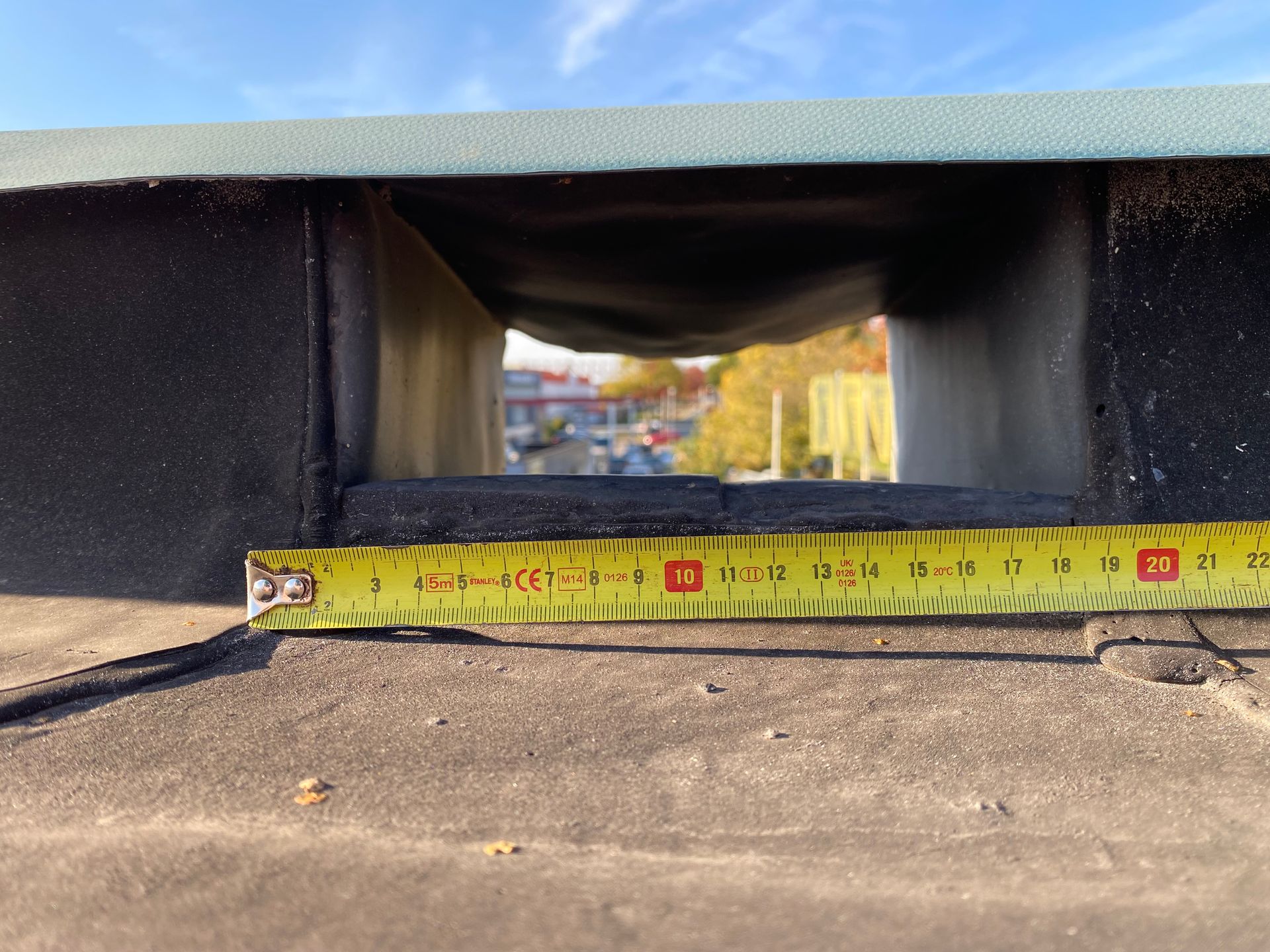 Een geel meetlint werd over de basis van een rechthoekige dakventilatieopening gelegd, waarop een breedte van ongeveer 20 centimeter te zien was.