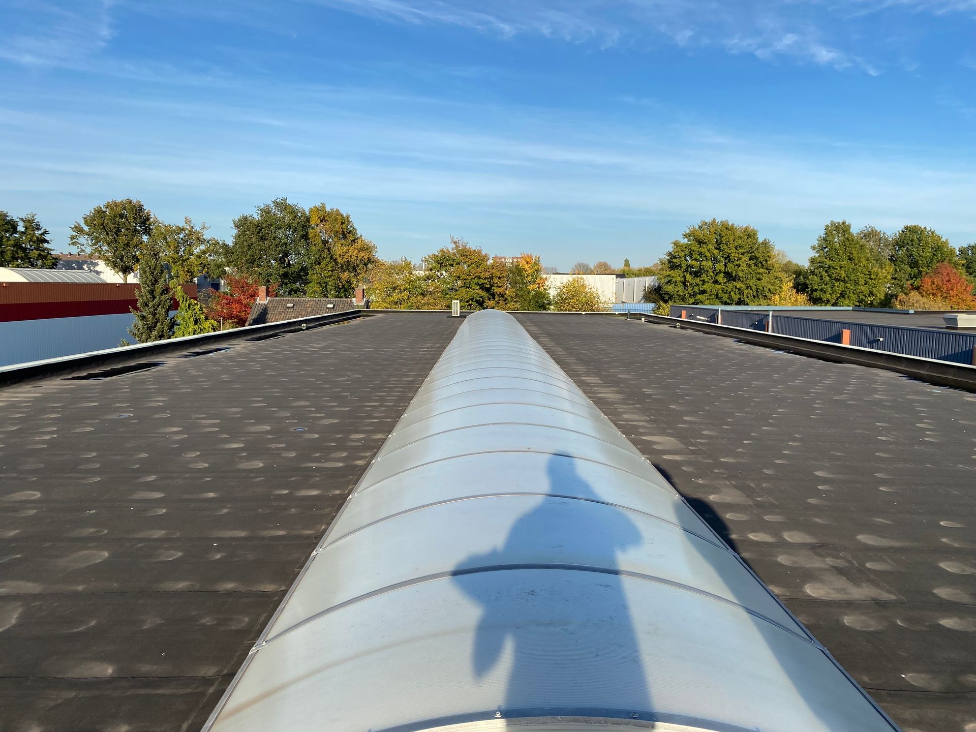 Een plat dak met een donker, gestructureerd membraanmateriaal en een lang, gebogen, doorschijnend dakraam in het midden.