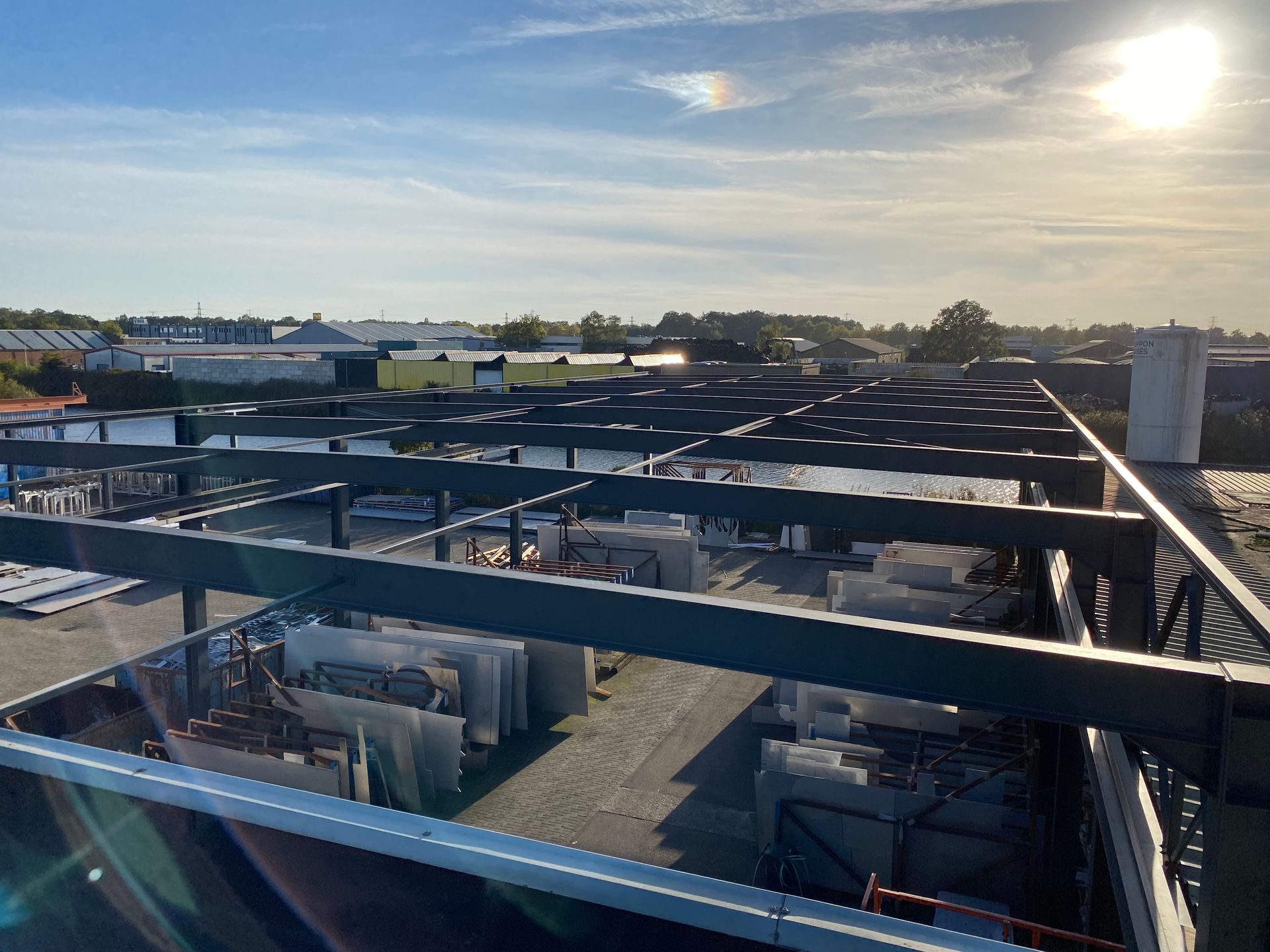 Een buitenterrein gevuld met grote stenen platen, opgestapeld onder een metalen overkapping, verlicht door fel zonlicht.