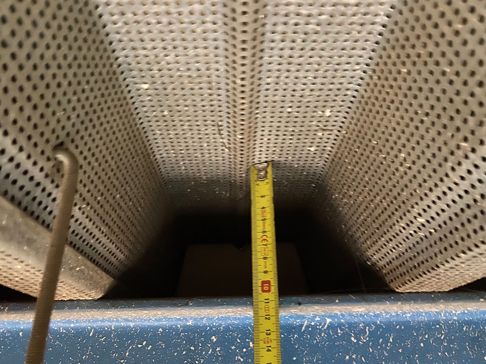 Een geel meetlint loopt naar beneden in de opening tussen twee geperforeerde metalen plafondpanelen.
