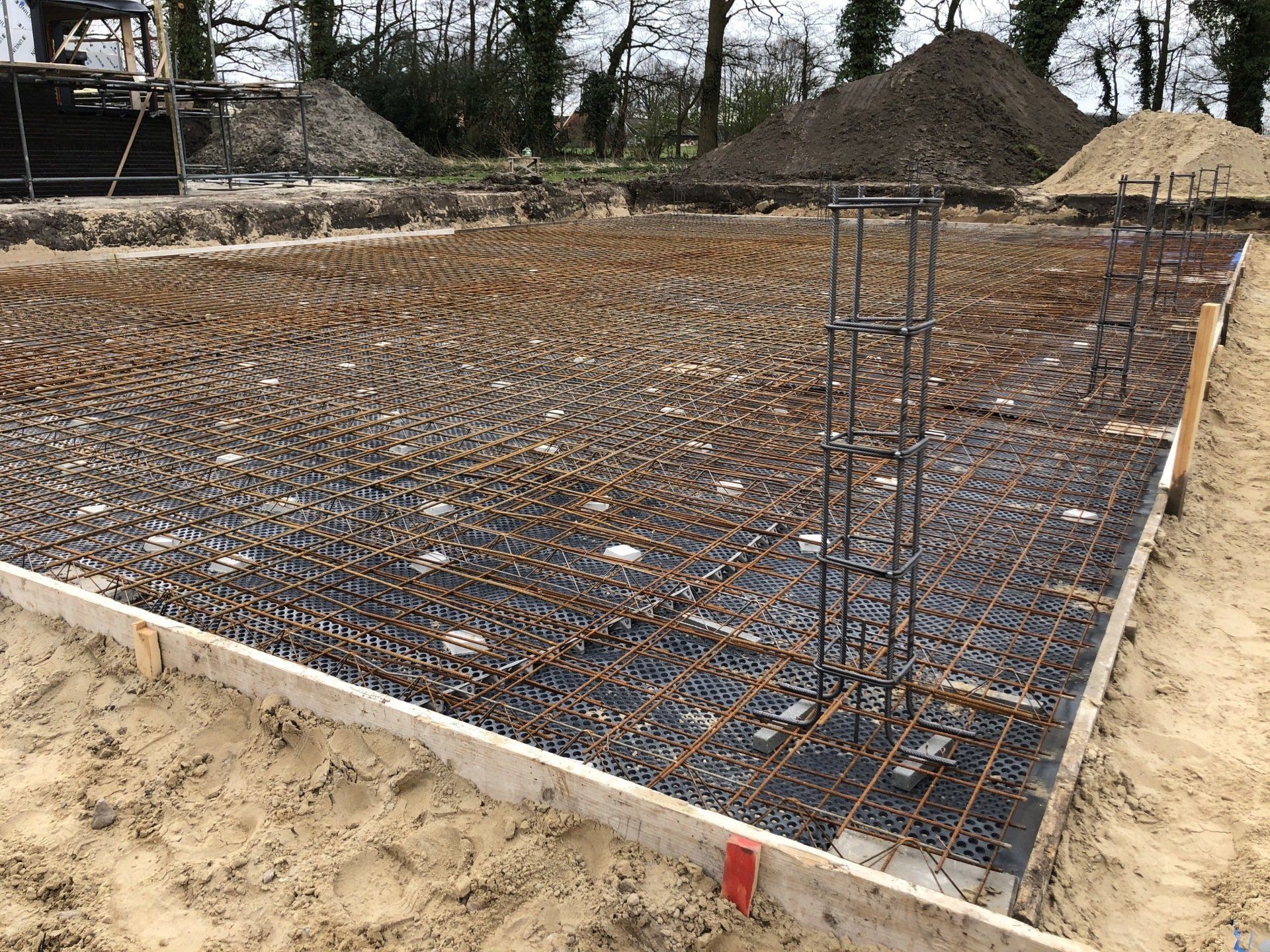Een funderingsplaat van gewapend beton met een stalen wapeningsnet en verticale kolommen, klaar voor het storten op een bouwplaats.