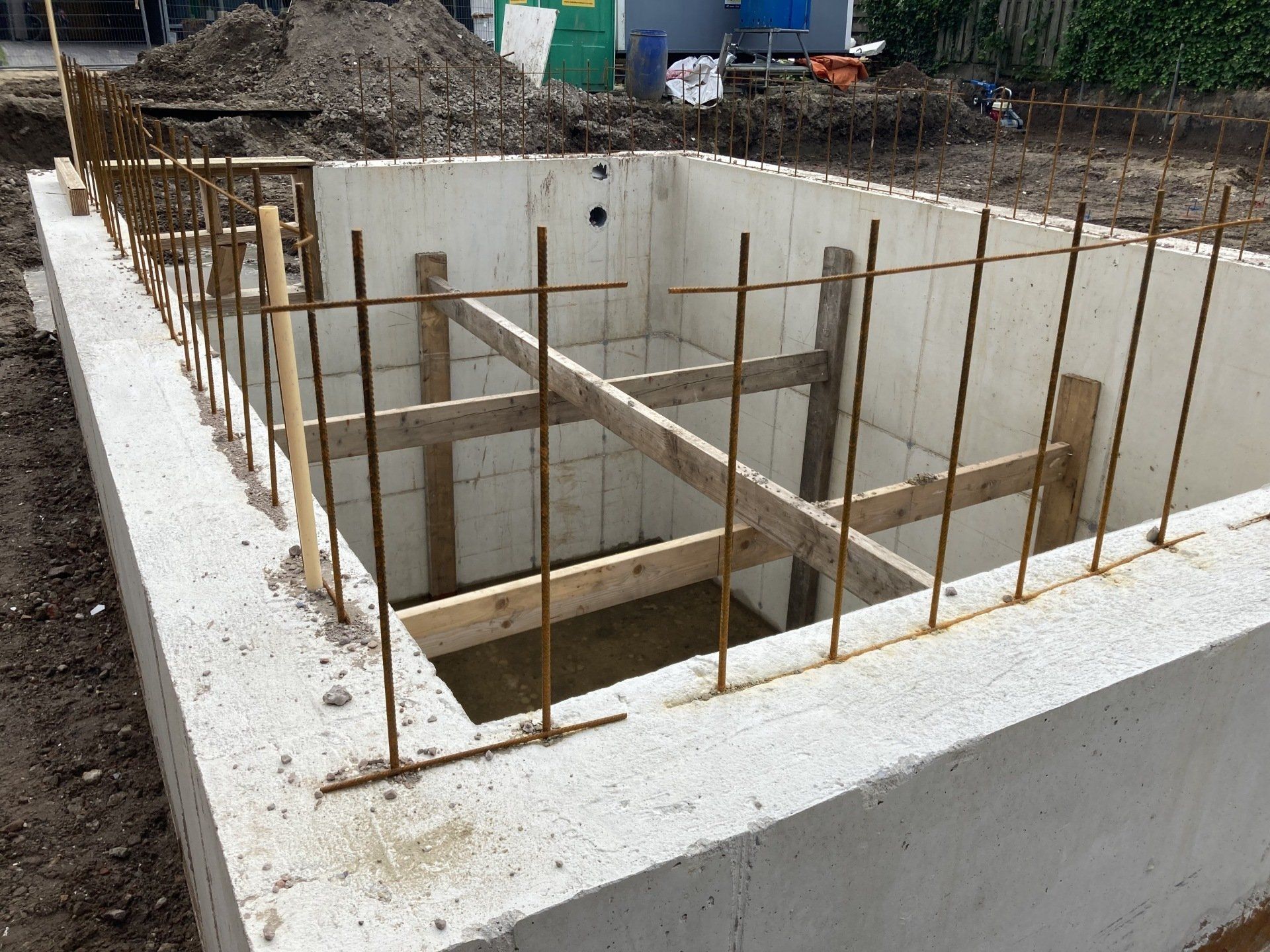 Betonnen funderingsmuren met verticaal naar boven gerichte wapeningsstaven, verstevigd door een houten binnenframe op een bouwplaats.