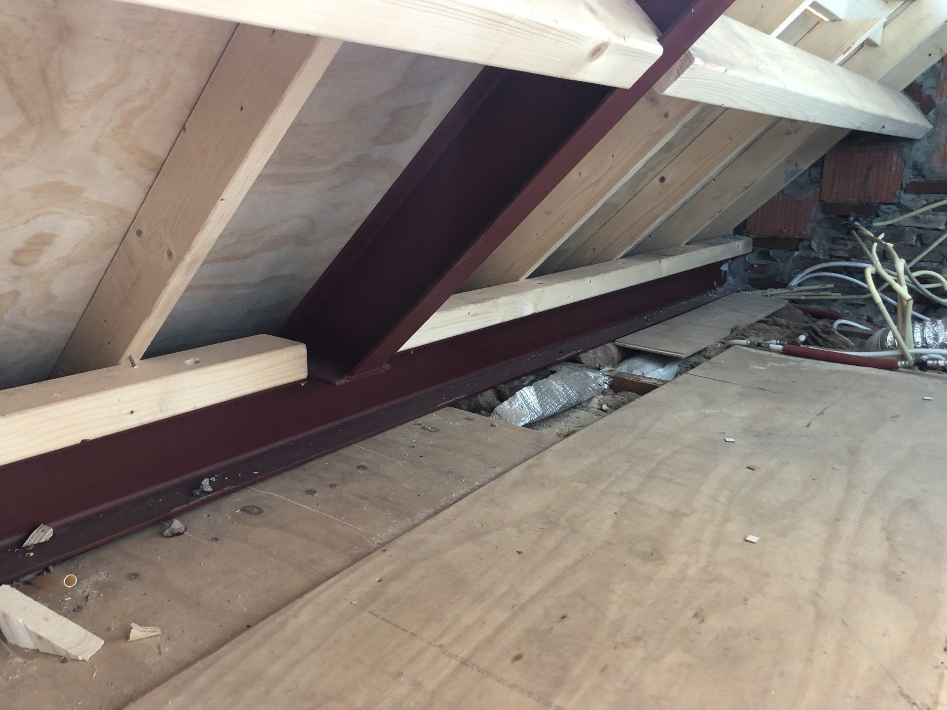 Een constructie bestaande uit een donkere metalen I-balk die houten spanten en multiplex beplating ondersteunt in een onafgewerkte ruimte.