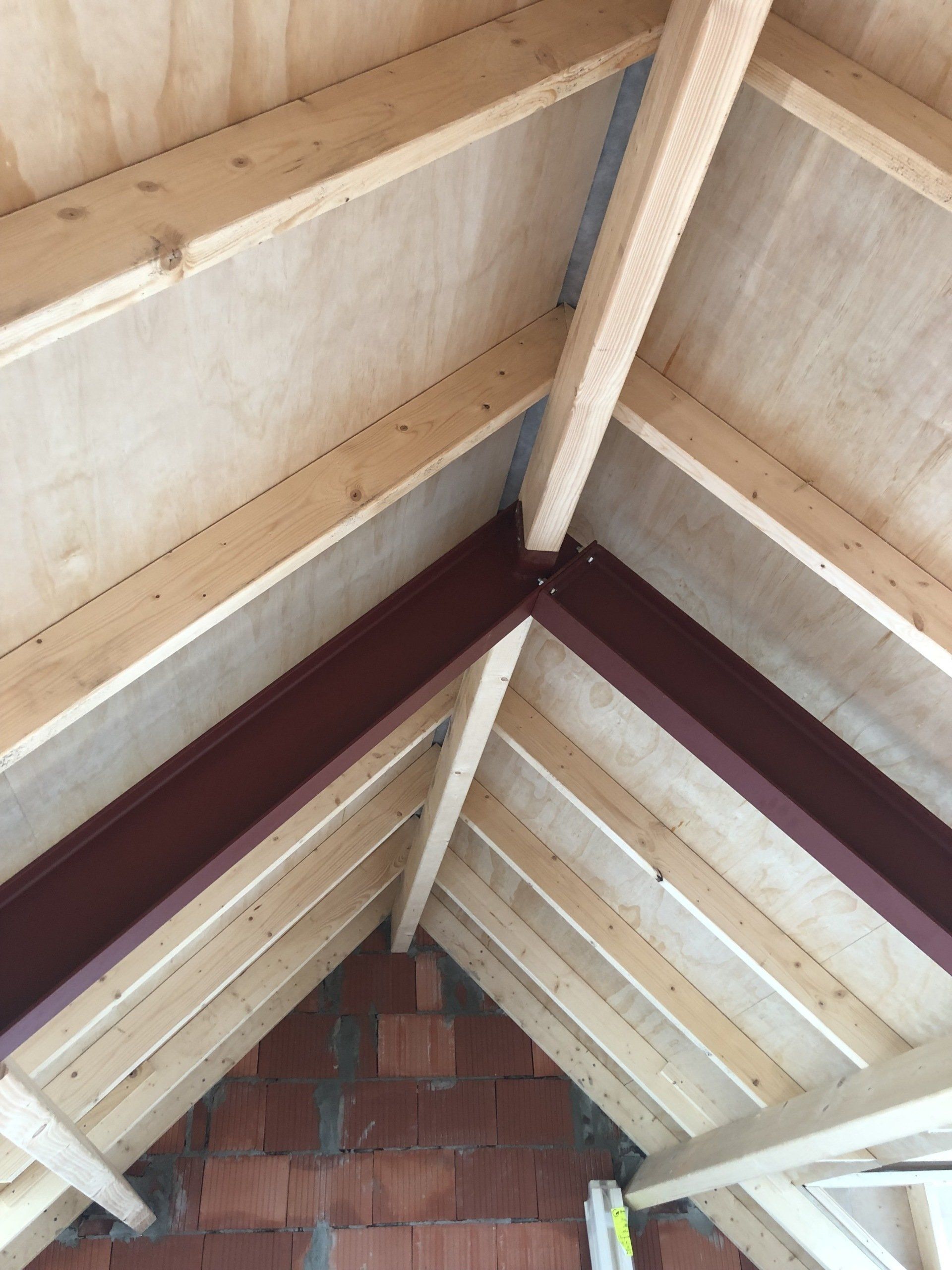 Een interieurfoto van een dak in aanbouw, met houten spanten, multiplex dakbeschot en een donkerbruine stalen balk.