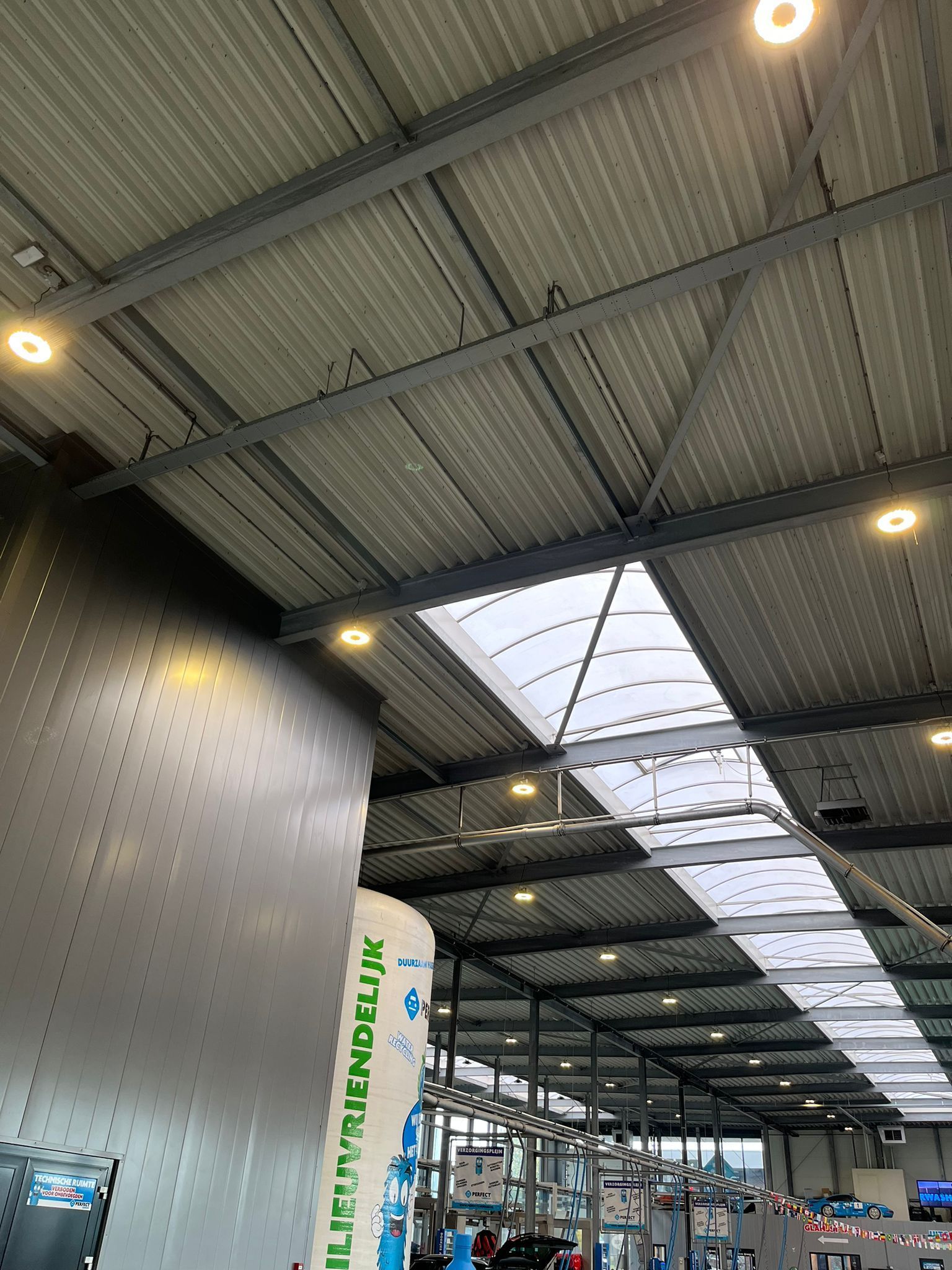 Interieurzicht omhoog naar een hoog, industrieel metalen plafond met inbouwverlichting en een lang, doorschijnend dakraam.