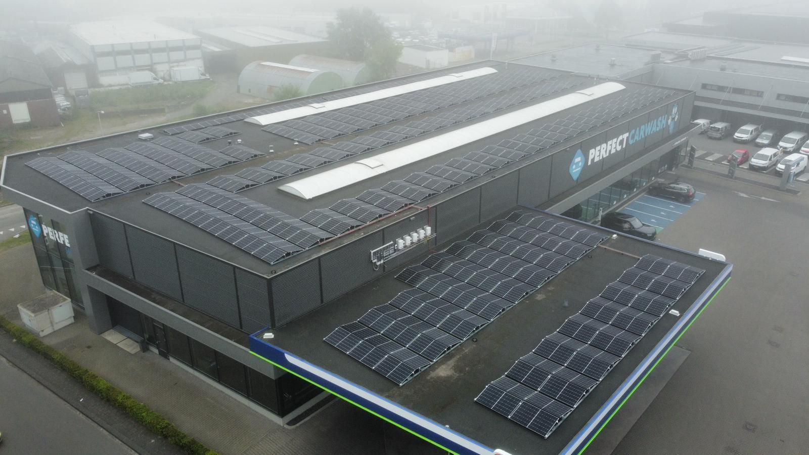 Luchtfoto van een bedrijfsgebouw met uitgebreide zonnepaneleninstallaties op het dak, genomen op een bewolkte dag.