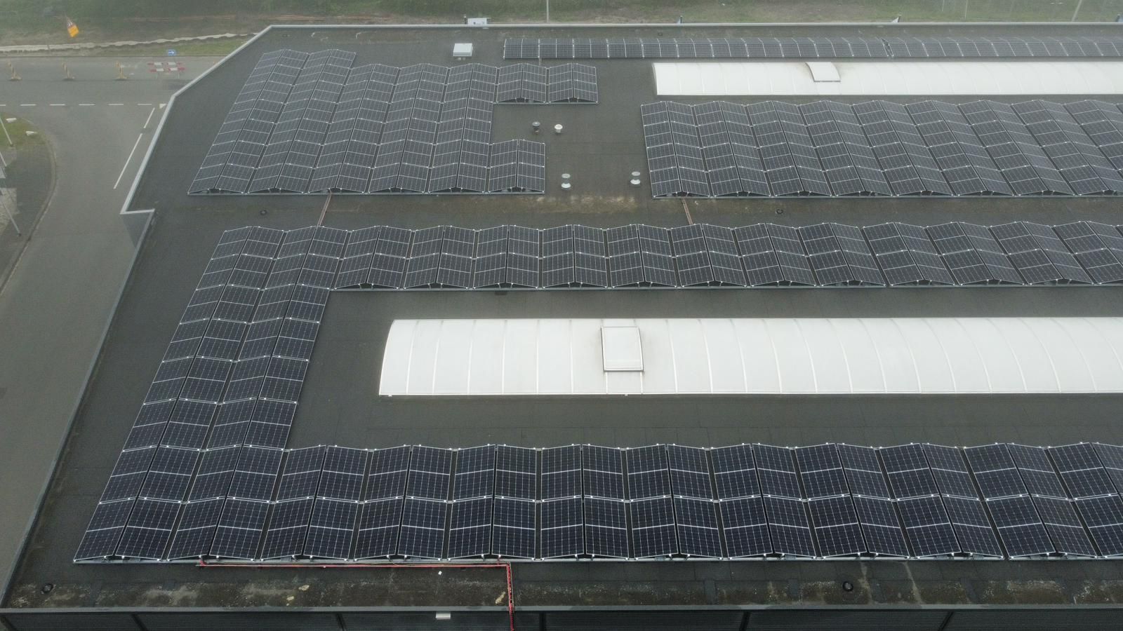 Luchtfoto van een groot, plat commercieel dak bedekt met rijen donkere zonnepanelen, afgewisseld met witte dakvlakken.