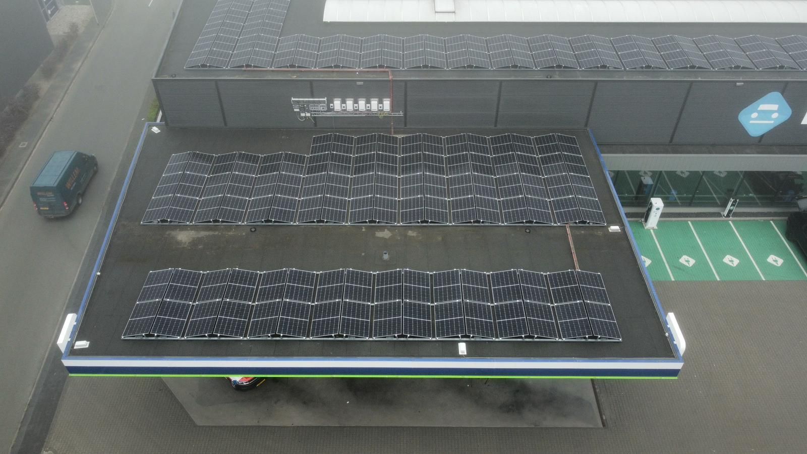 Een opname vanuit een hoog perspectief van het dak van een modern gebouw, met twee rechthoekige rijen zonnepanelen op een zwarte ondergrond.