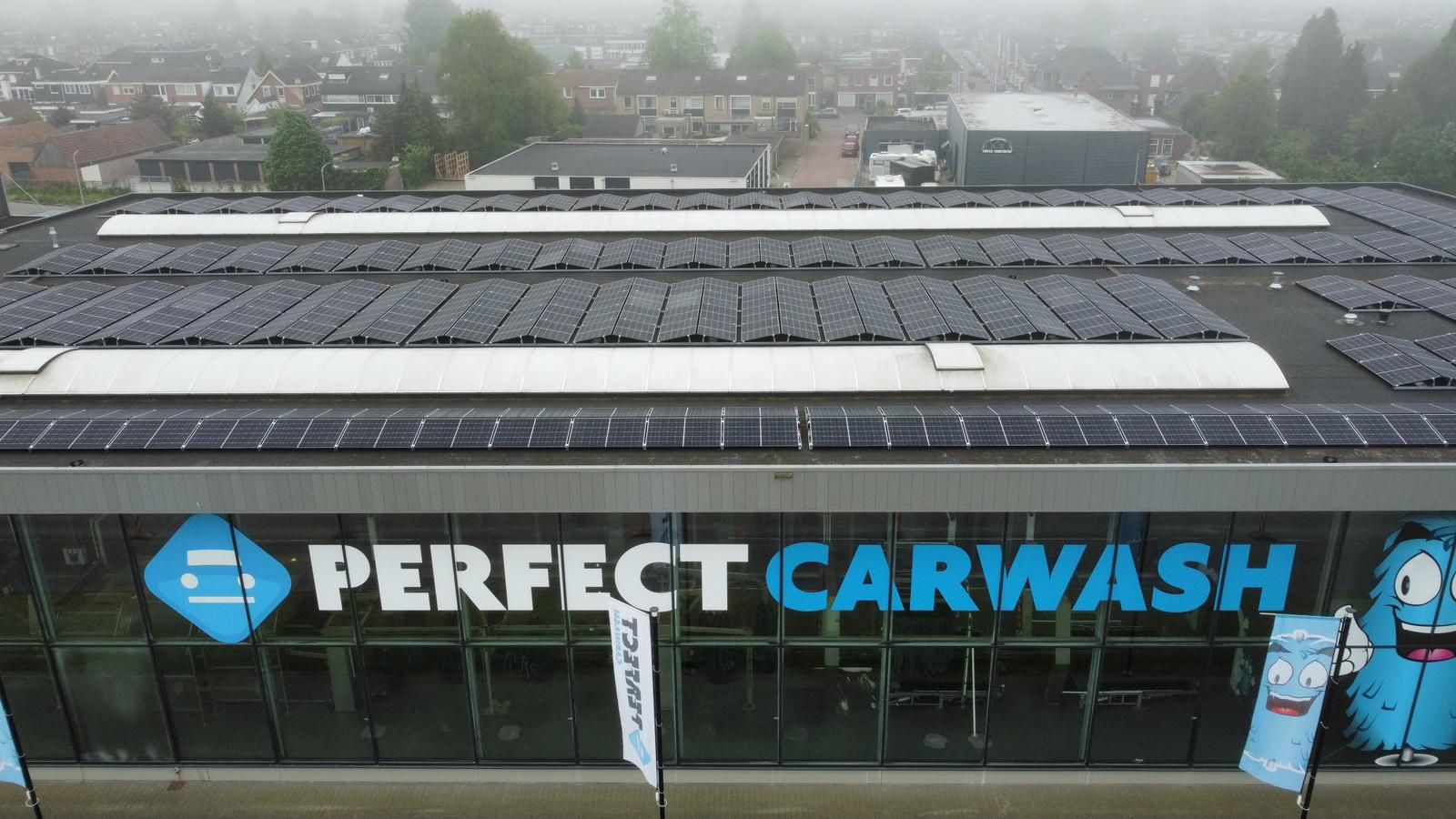 Exterieurfoto van een Perfect Carwash-gebouw met zonnepanelen op het platte dak en grote reclameborden op de glazen gevel.