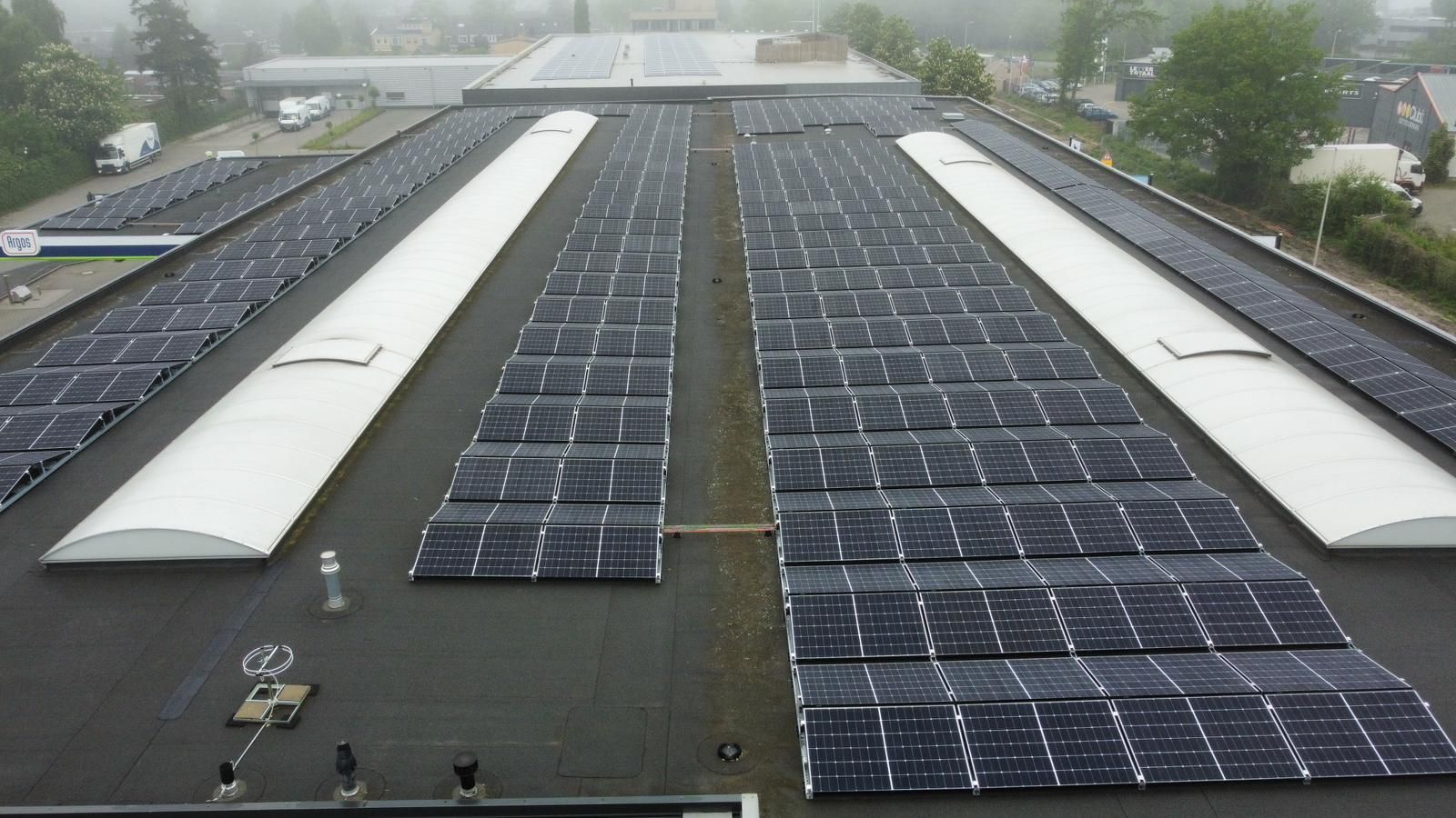 Een verhoogd zicht op een plat commercieel dak bedekt met talloze zwarte zonnepanelen, gescheiden door witte stroken dakramen.