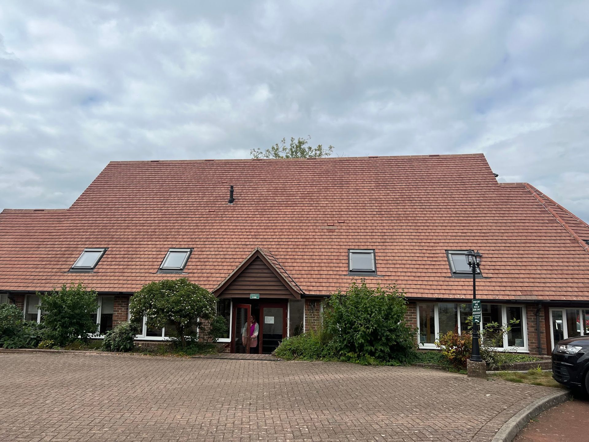 Building with red tile roof, windows, and entrance; cloudy sky overhead.