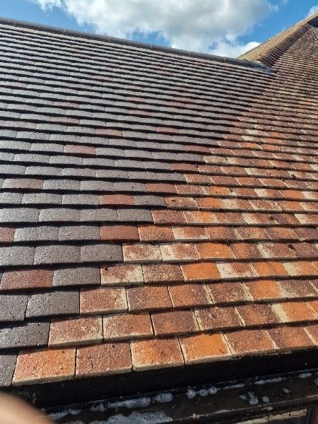 Roof tiles, half cleaned, showing a contrast in color from brown to orange under a partly cloudy sky.