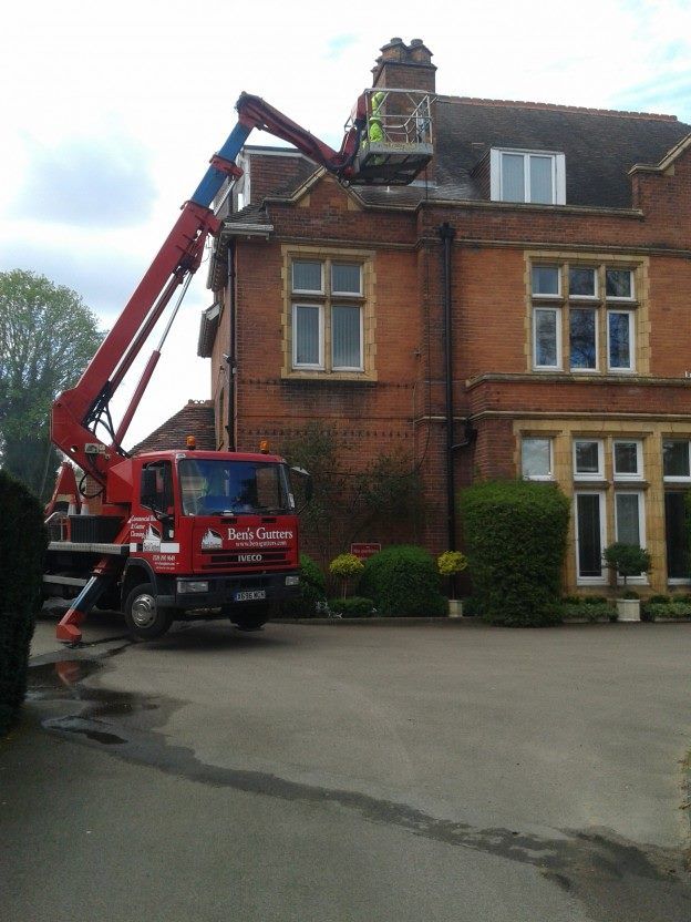 A cherry picker truck with a worker at the chimney of a brick building.