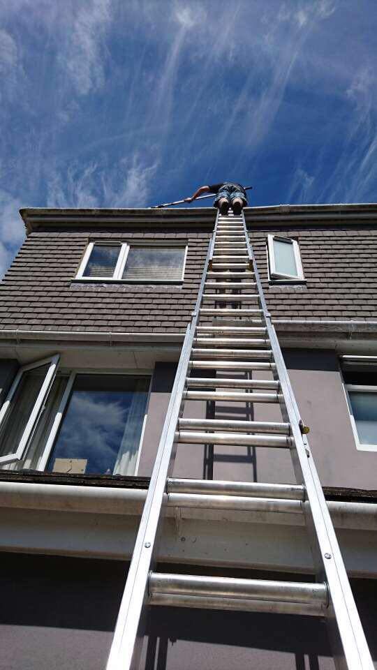 Person on ladder cleaning gutters of a two-story house, blue sky background.