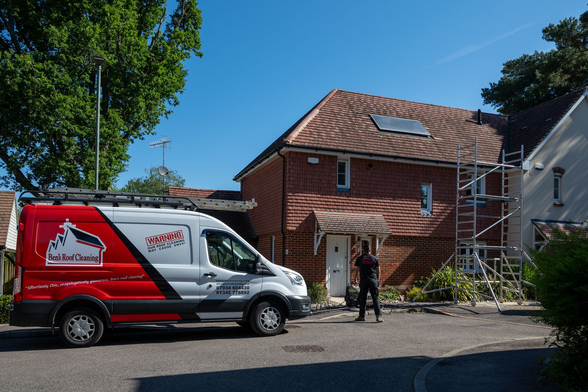 Red and white van parked in front of a brick house with scaffolding; person standing by the door.