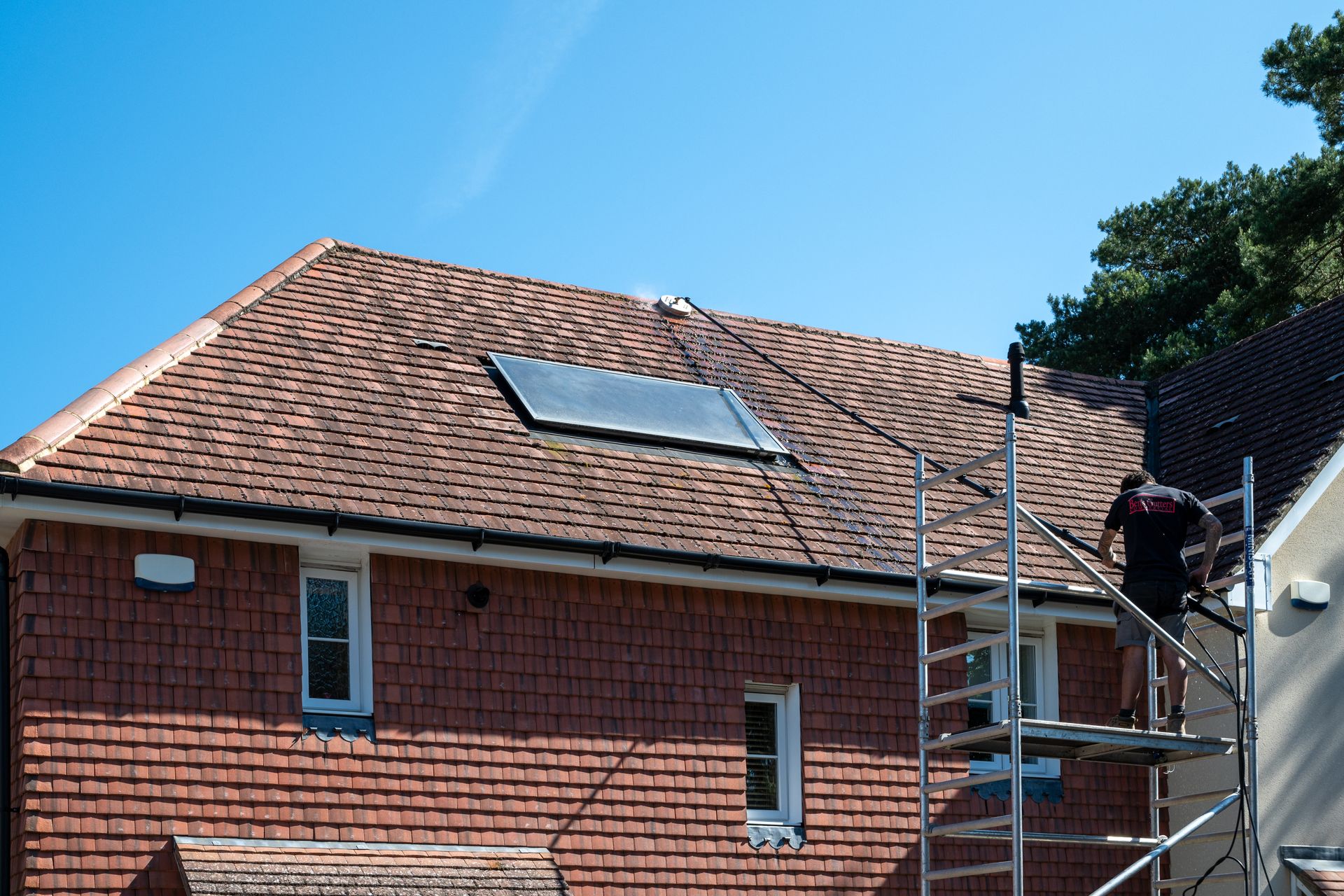 A person on scaffolding working on a roof with solar panel on it, blue sky background.