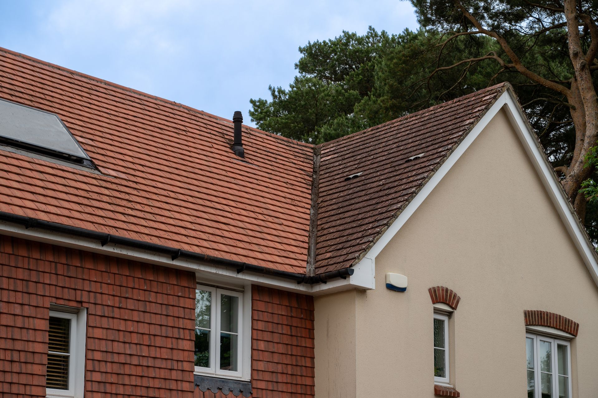 Red tile roof on brick and beige-walled buildings against a cloudy sky.