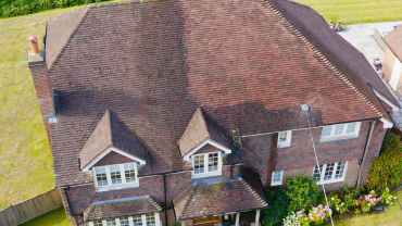Brown-tiled roof of a two-story brick house with dormer windows and a grassy lawn in the background.