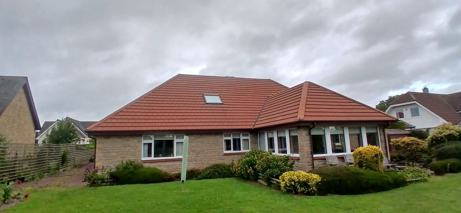 A red-roofed brick house with a green lawn under a cloudy sky.