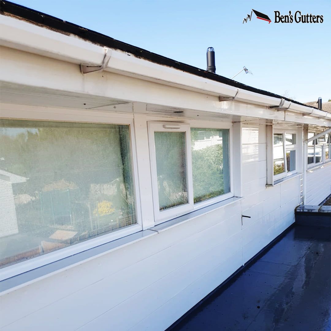 White building exterior with windows and a black flat roof under a blue sky.