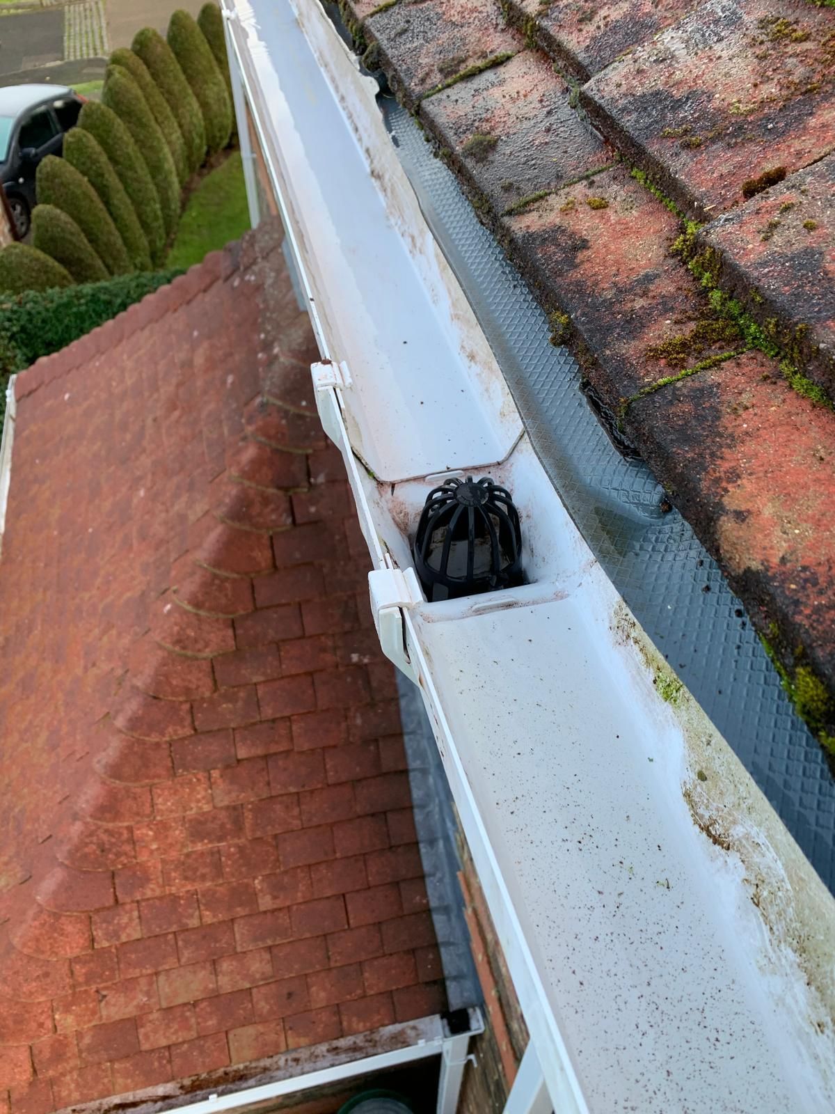 White gutter with a black downspout guard, alongside a red tile roof.