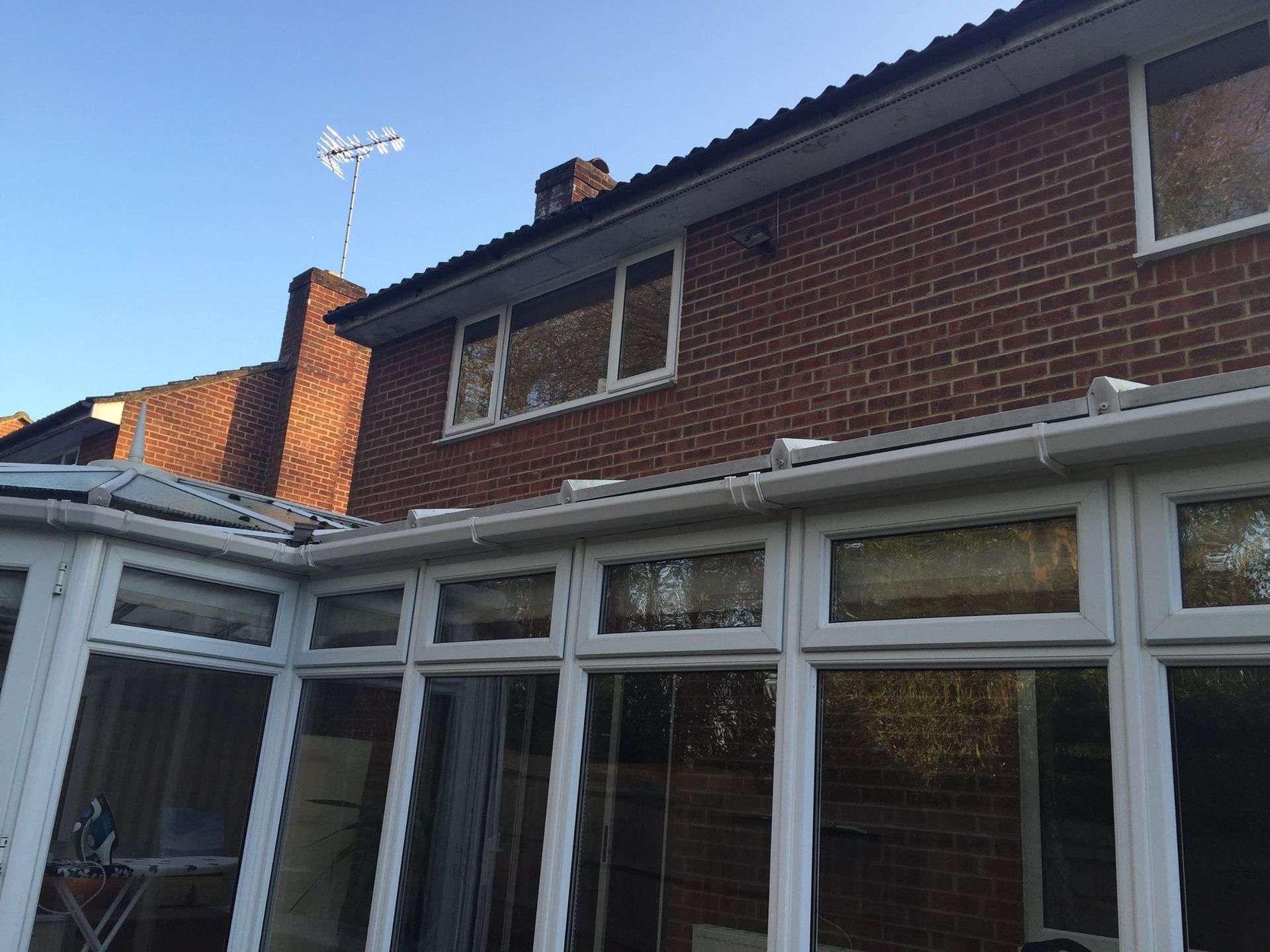 Exterior view of a brick house with a white-framed conservatory. Clear blue sky is visible.