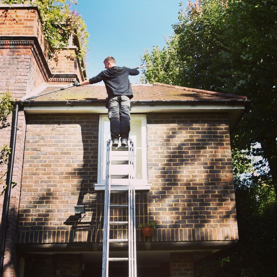 Man on ladder reaching onto roof of brick building. Sunny day.
