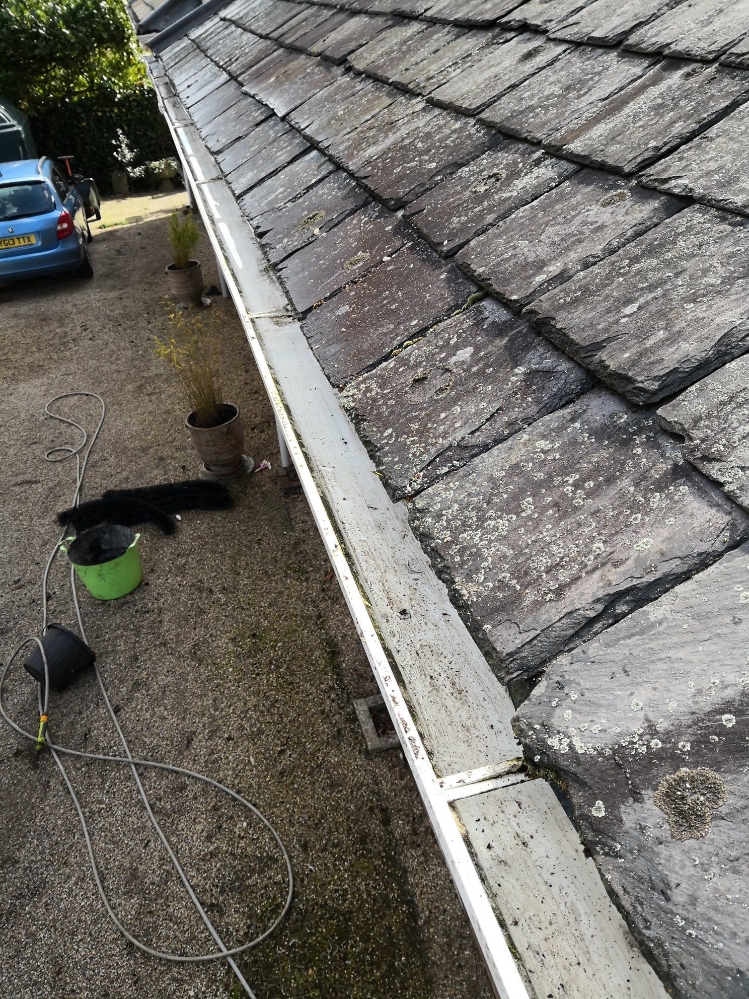Gray roof tiles and gutter with debris, near a driveway and vehicle.