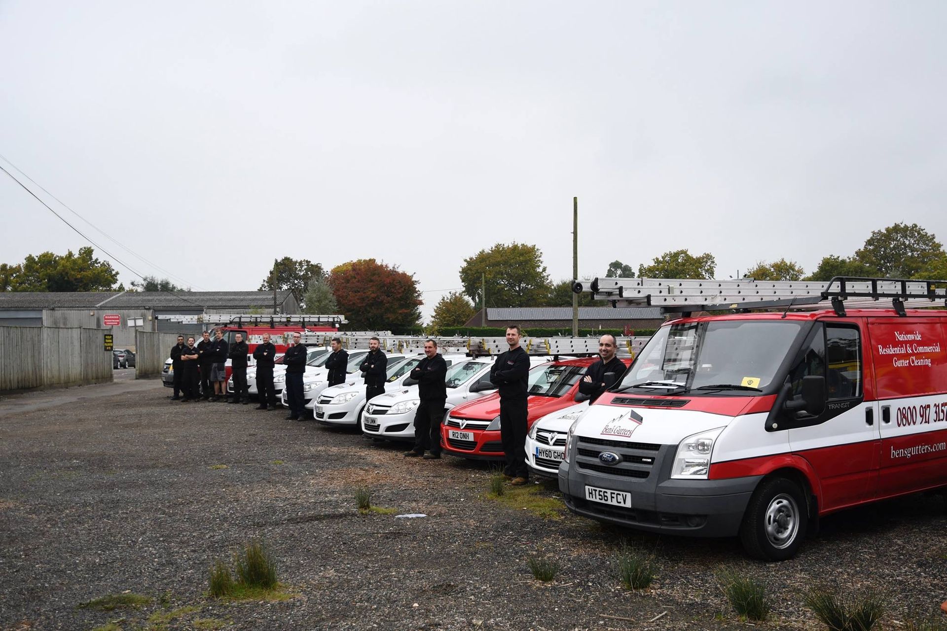 Emergency vehicles and personnel standing on a gravel lot under a cloudy sky.